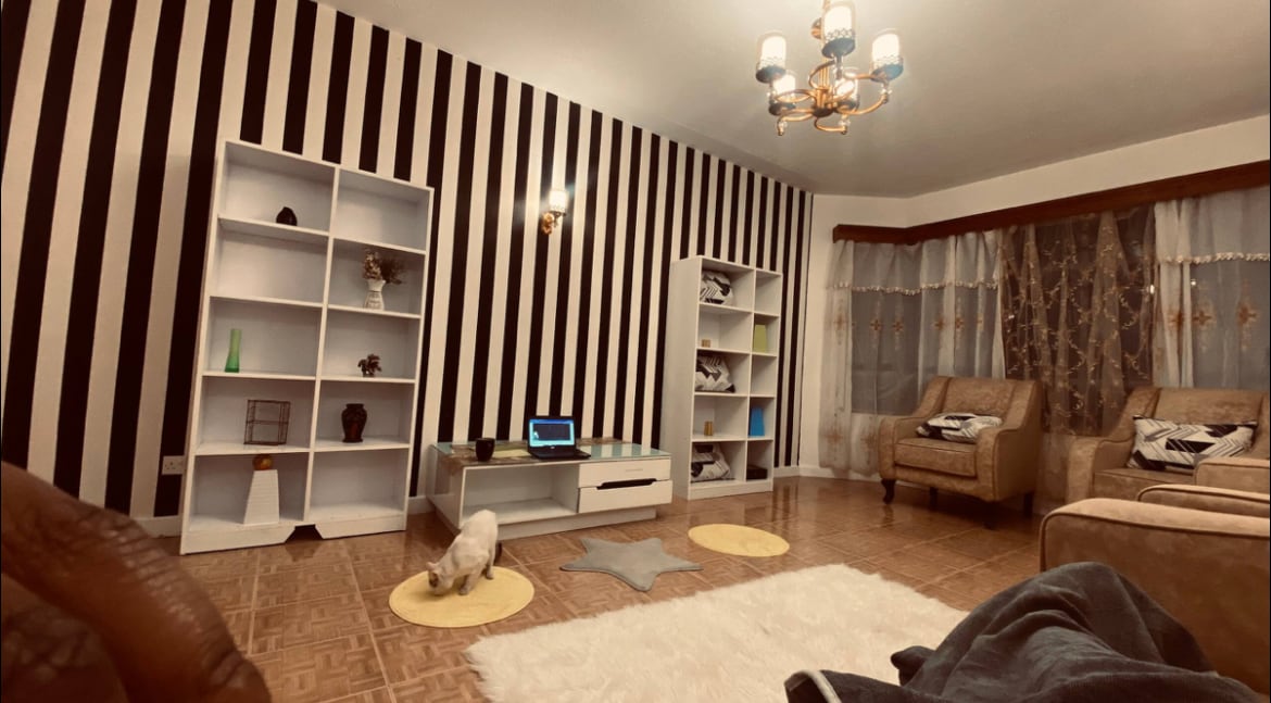 A living area features a striped wall design in black and white, complemented by a soft rug in the shape of a star. Two armchairs are placed on opposing sides, while a low coffee table sits centrally. A laptop rests on the table, and a light fixture hangs above.