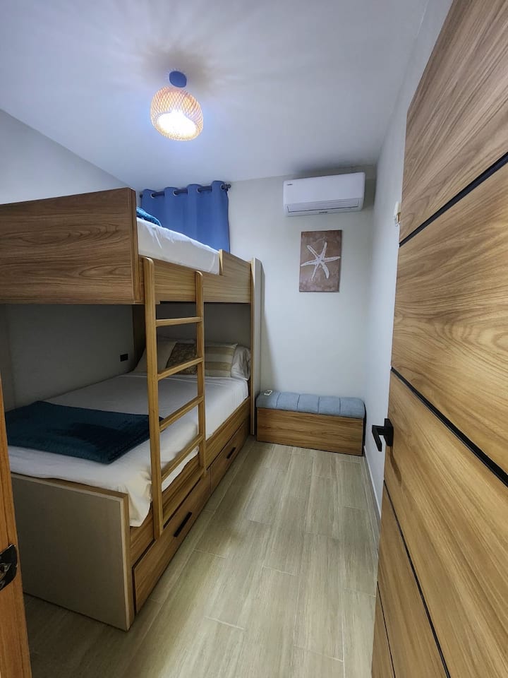 Segunda habitación con una litera en madera de plazas (full) , colchones cómodos y línea de cama nueva. Almacenamiento en la parte inferior de la literal y también al abrir la Bufetera.  Aire acondicionado. 