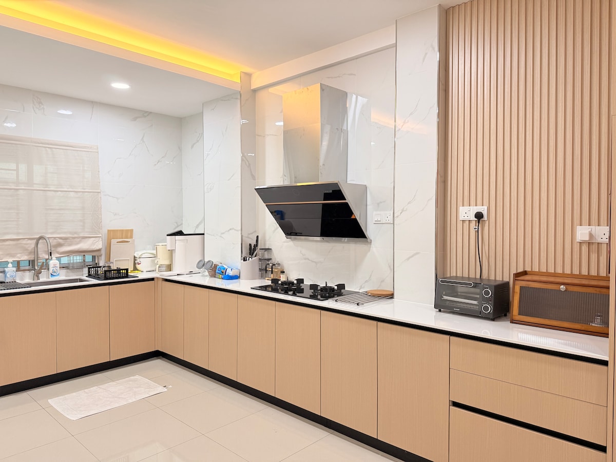 An open-concept kitchen features sleek cabinetry with a warm finish. A large, modern gas stove is set against a marble backsplash. Ample counter space is available, complemented by under-cabinet lighting. Essential appliances, including a microwave and coffee maker, are neatly arranged on the countertop.
