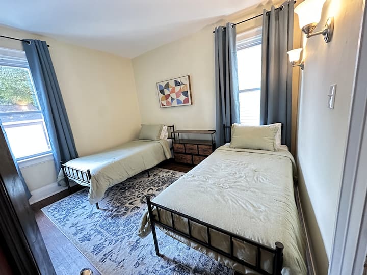 Dormitorio luminoso con dos camas individuales XL, un tocador con estaciones de carga integradas y un armario. Perfecto para amigos o familiares que buscan comodidad y conveniencia durante su estancia en Buffalo.