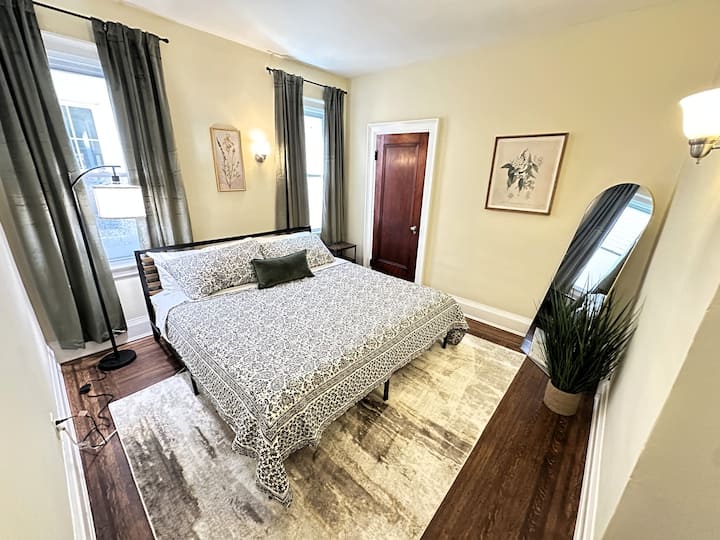 Elegante dormitorio con una cómoda cama tamaño king, cortinas opacas, lámparas de lectura y una mesita de noche con una estación de carga integrada. Un amplio armario completa este acogedor y relajante refugio después de un día explorando Búfalo.