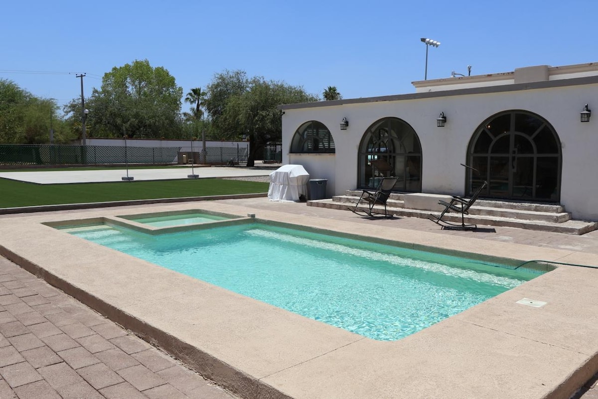 A private pool area is captured, featuring a clear turquoise pool with a shallow section. Surrounding the pool, a patio is installed with stone tiles, and lounge chairs are positioned for relaxation. The background reveals an expansive lawn area, well-maintained and inviting.