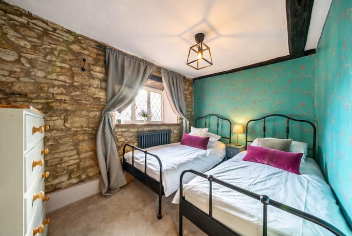 In deze kamer staan twee eenpersoonsbedden tegen een muur van zichtbare stenen en met jade behang.