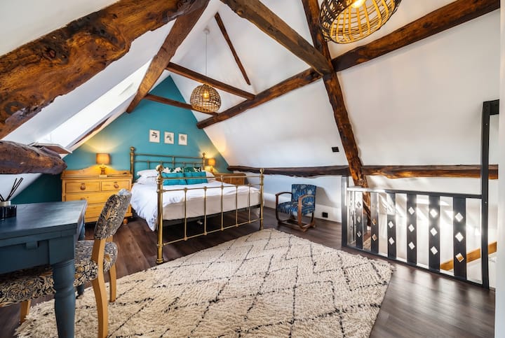 Het mezzanine tweepersoonsbed heeft een messing bed onder hoge balken met groenblauwe accenten.