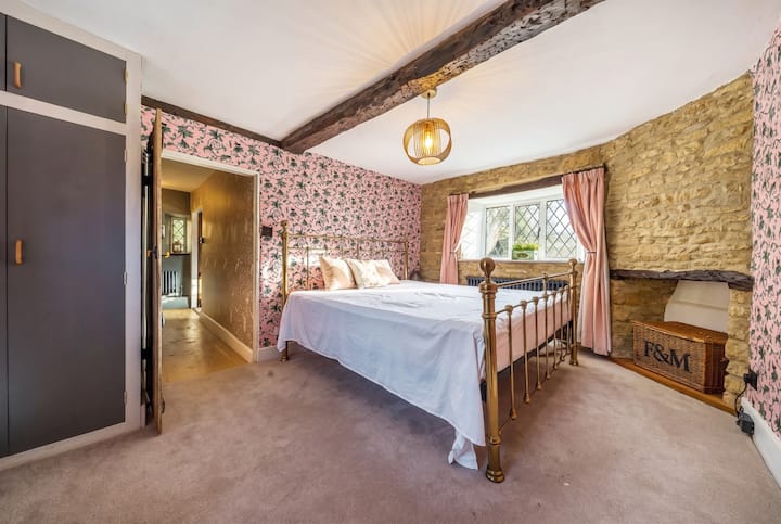 Deze tweepersoonskamer heeft een messing bed, muren met een rozenprint en Cotswold-stenen bij het raam.