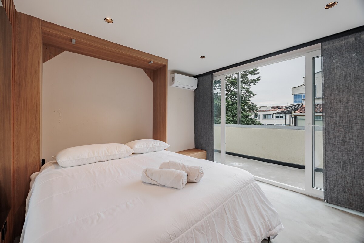 Un dormitorio bellamente diseñado con una cama tamaño king, una gran ventana y un balcón privado. Luminoso, elegante y cómodo, ofrece un ambiente sereno con detalles refinados y excelente luz natural.