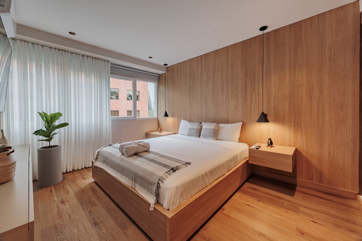 Un dormitorio bellamente diseñado con una cama tamaño king y ventanas con impresionantes vistas a la ciudad. Luminoso, elegante y cómodo, ofrece un ambiente sereno realzado por detalles refinados y una excelente luz natural.