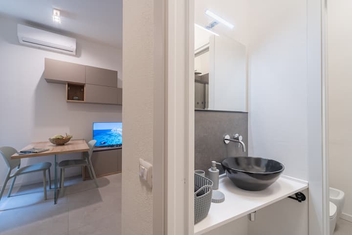 Espacio habitable moderno y espacioso. Una mesa de comedor para 4, una televisión inteligente, una lámpara de diseño y cuadros minimalistas completan el entorno. Perfecto para relajarse después de un día en la playa o en la ciudad.