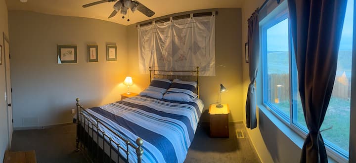 Second bedroom with queen bed and brass frame, 2 side tables with lamps and large window. 