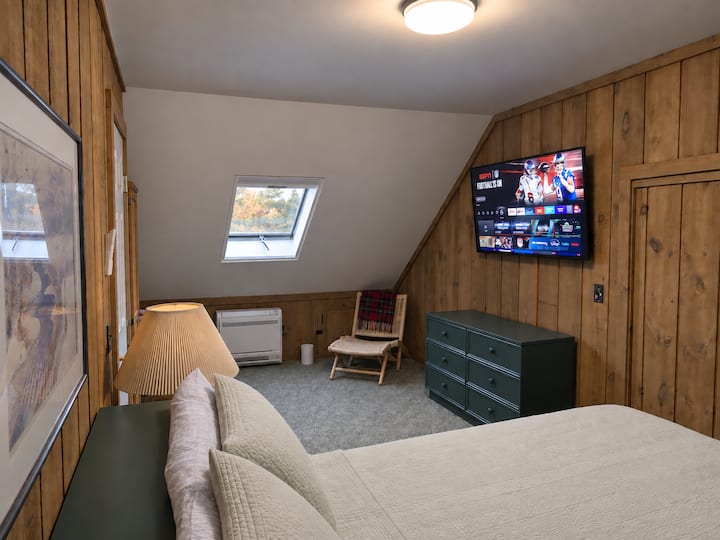 Comfortable queen bed with a wall-mounted smart TV, skylight with a blackout curtain, and a full bathroom just steps away.