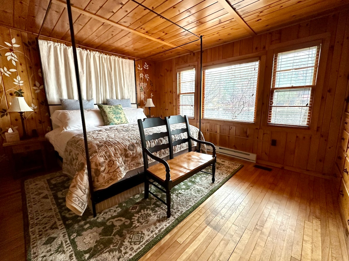 The Ivy Room: A cozy king suite with golden pine walls, hand-painted ivy, soft lamplight, and a canopy bed—your peaceful retreat in the Adirondacks for rest, romance, and slow mornings.