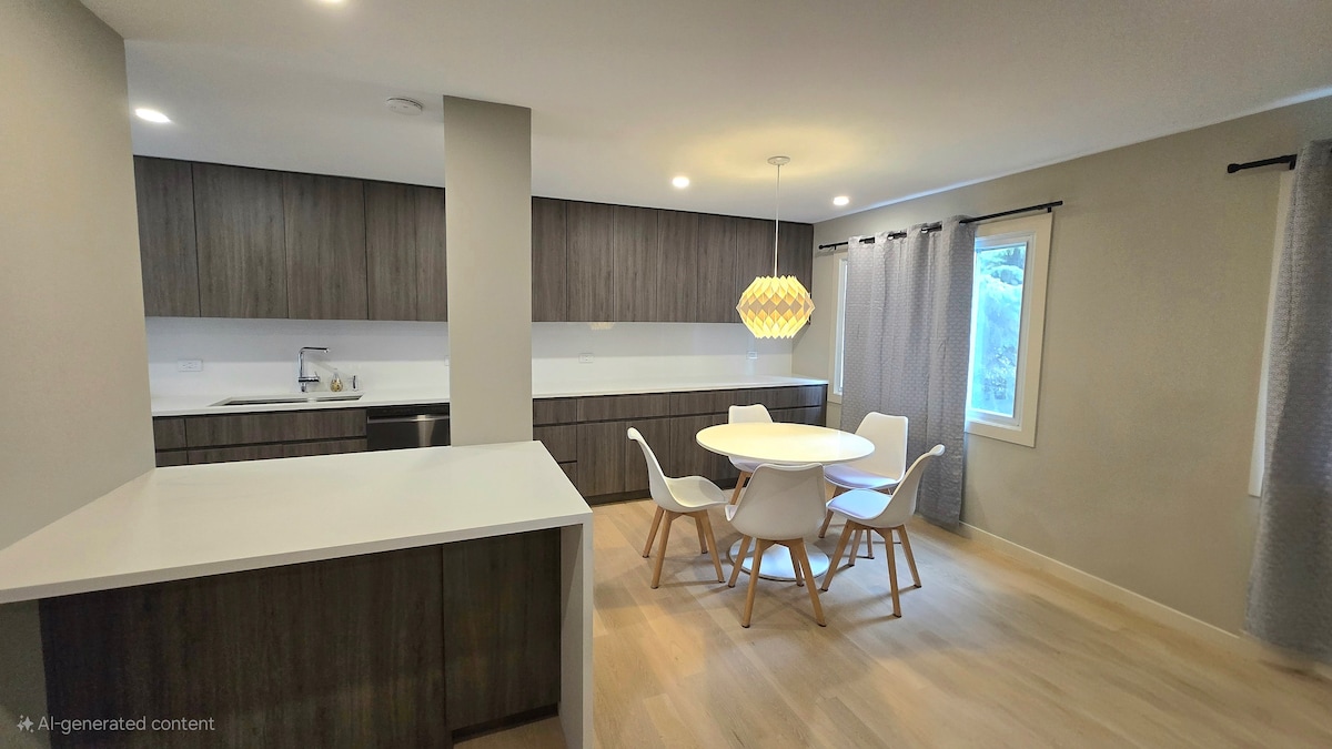 A modern kitchen and dining area features sleek cabinetry in deep wood tones. A round dining table with white chairs is illuminated by a unique pendant light. Natural light filters through a window, while curtains add a soft texture to the space.