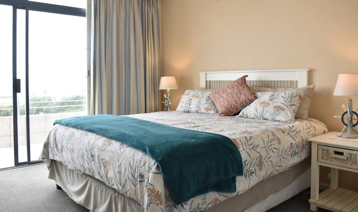 Главна спалня с изглед към океана и достъп до балкона.