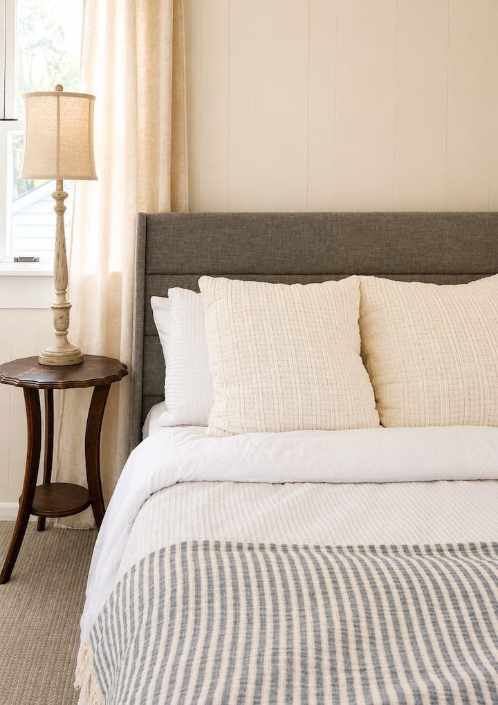 Private suite detached from the main house with balcony or driveway access. Features a kitchenette, dining table for two, sofa, TV, double bed, closet storage, and full bath with shower.