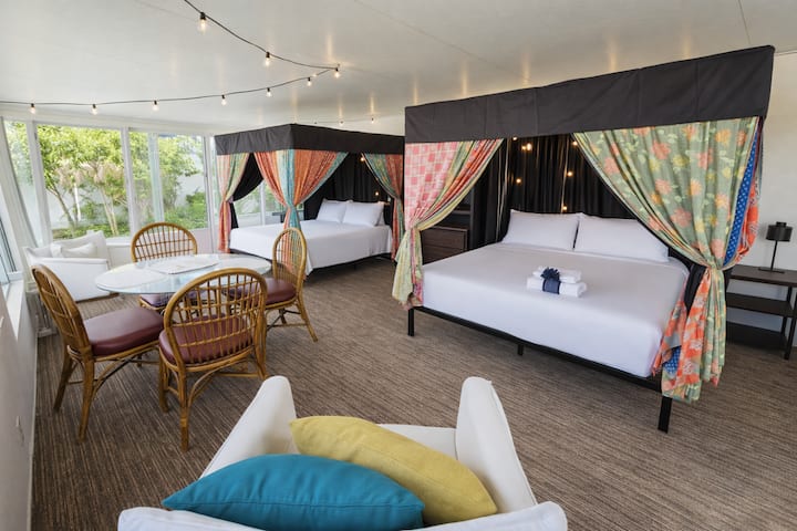 - Two plush beds framed by colorful fabric create a festive glamping style space
- Indoor sitting area with dining table is perfect for casual meals or card games
- Surrounded by windows, this cheerful room invites nature right inside