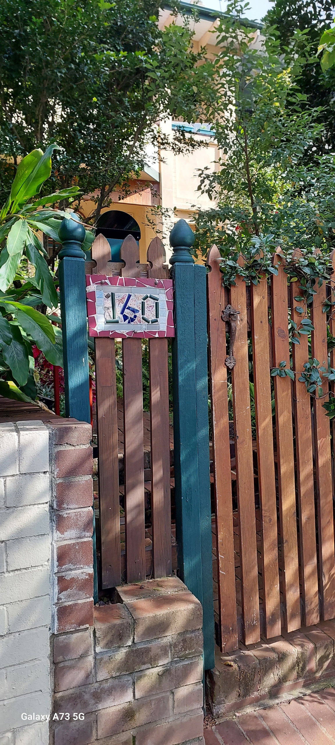 A charming entrance is highlighted by a wooden gate and a brown picket fence, adorned with lush greenery. The property number '160' is displayed on a colorful sign, adding a welcoming touch to the space.