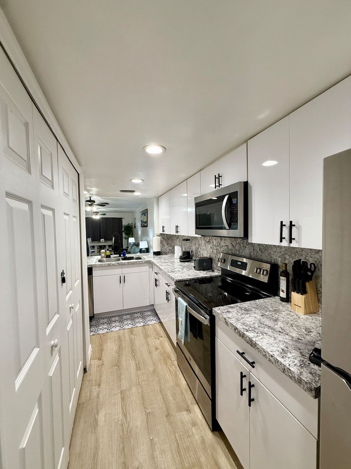 A modern kitchen is featured with sleek cabinetry and granite countertops. Stainless steel appliances, including an oven and microwave, are positioned for convenience. Soft lighting illuminates the space, while a patterned tile backsplash adds a subtle detail. Ample storage is provided with several closed cabinets.