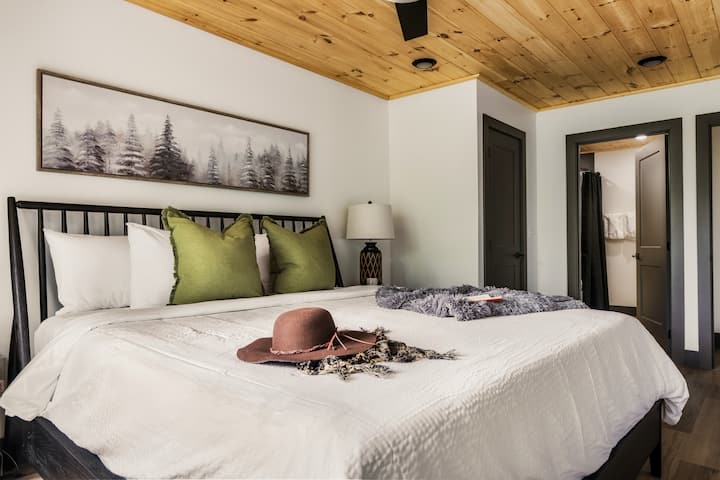 Une autre chambre au lit très grand lit magnifiquement conçue pour un confort ultime. Détendez-vous sous de chauds plafonds en planches de bois avec un matelas moelleux, des oreillers décoratifs doux et des œuvres d'art élégantes sur la nature. Offre un accès direct aux salles de bain et aux espaces de vie à proximité.