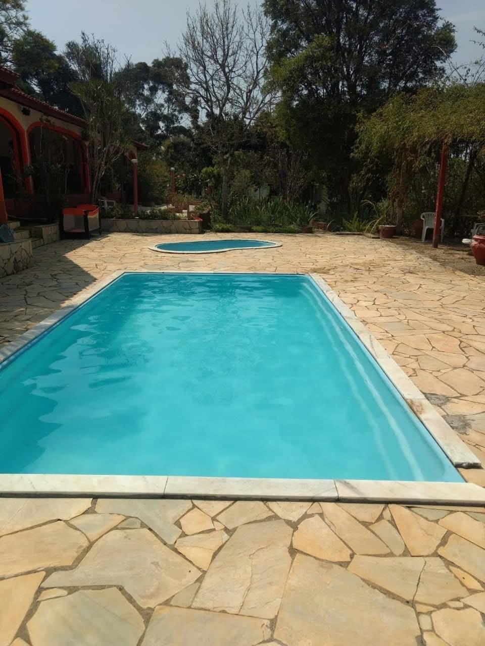 The image showcases two swimming pools, one designed for adults and the other for children. The pools are framed by a stone patio and surrounded by various greenery, offering a natural setting that integrates with the landscape.