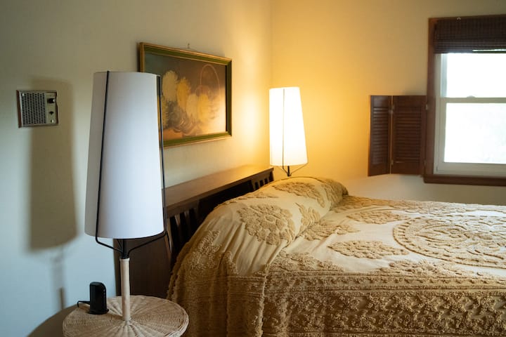 Chumba cha kulala cha Queen cha ghorofa ya juu. Chumba hiki cha kulala kina meza mbili zilizo na taa kwenye kila moja na vituo vya kuchaji. Kuna mito 6, feni ya kusimama na rafu mbili za mizigo. Madirisha yana vivuli vyeusi. Pia kuna televisheni ya inchi 43.