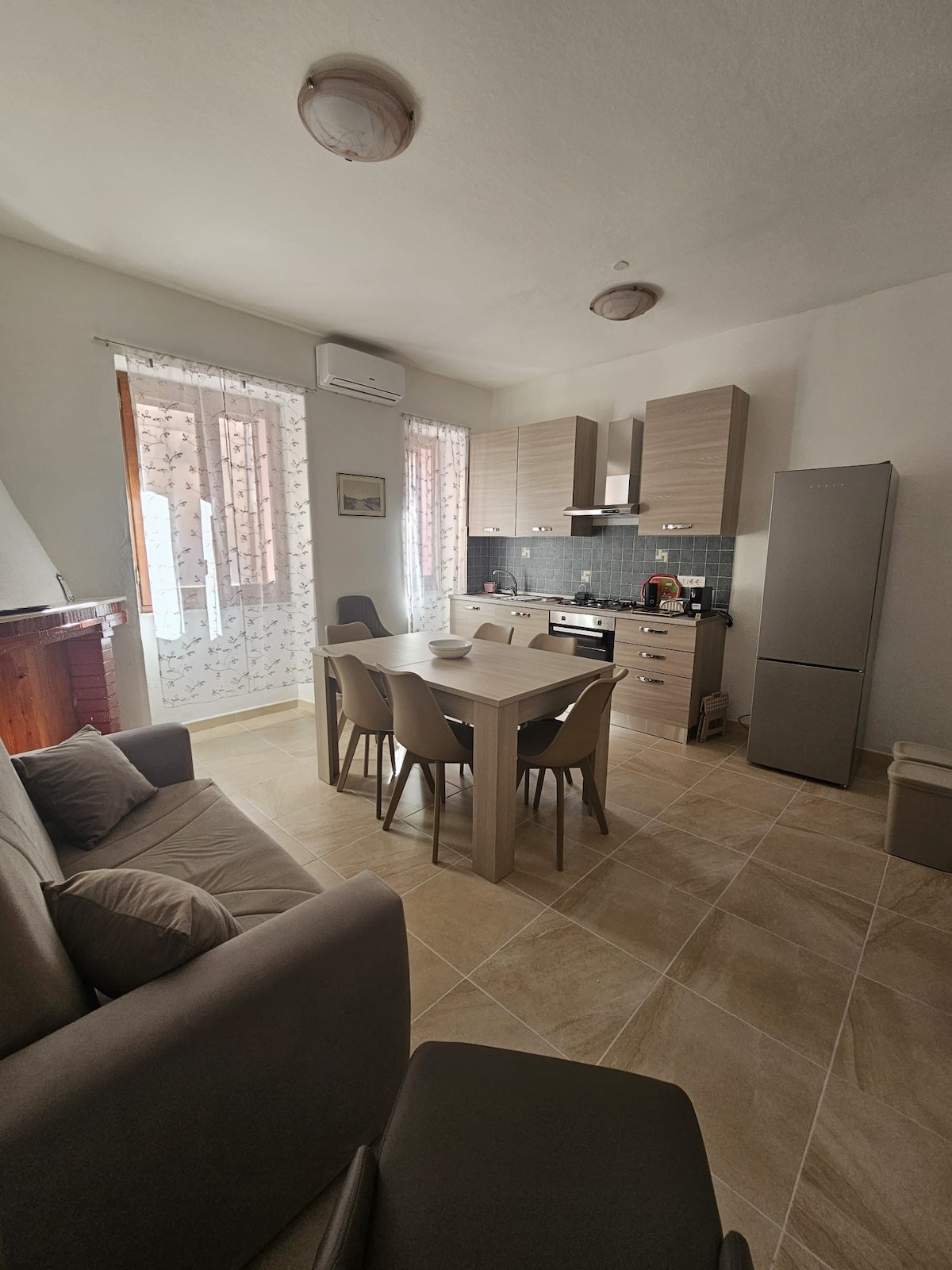 A well-equipped kitchen area is shown, featuring light wood cabinetry and a modern stove. A dining table with four chairs sits in the center, complemented by a comfortable sofa in the corner. Natural light streams through the window, enhancing the inviting ambiance.