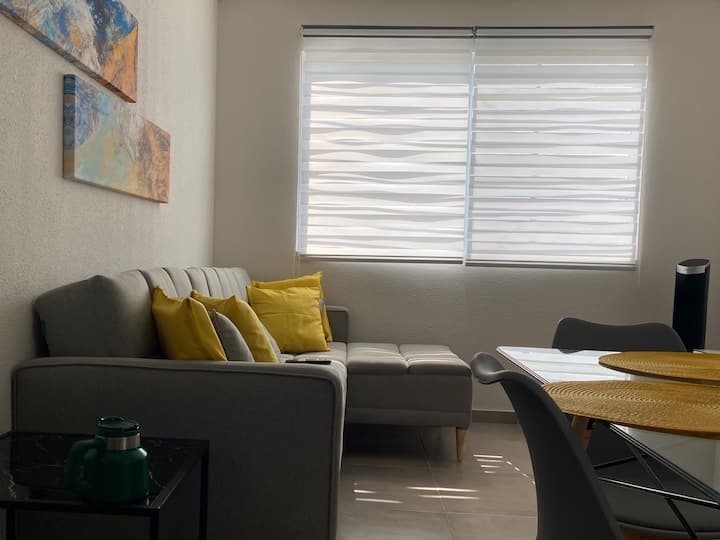 Ნათელი ოთახი გასაშლელი დივნით ნეიტრალურ ტონებში და ყვითელი ბალიშებით, რომლებიც თბილ და თანამედროვე შტრიხებს ქმნის.