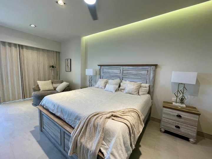 Prostrana spavaća soba s bračnim krevetom, izravnim pristupom kupaonici i garderobom, pametnim televizorom od 65", električnim radnim stolom, okretnom stolicom za odmor i razmišljanje o pogledu na more