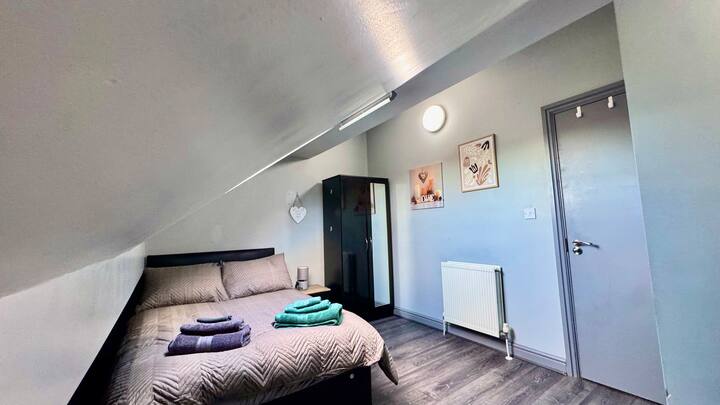 Chumba cha kulala cha starehe kilicho na kitanda cha watu wawili, mashuka safi ya kitanda, uhifadhi wa kutosha wa nguo, viango, mfumo wa kupasha joto, pasi na vivuli vyenye giza chumbani kwa ajili ya kulala usiku kwa utulivu. Imebuniwa ili kutoa kila kitu unachohitaji kwa ajili ya ukaaji wa kupumzika na rahisi.