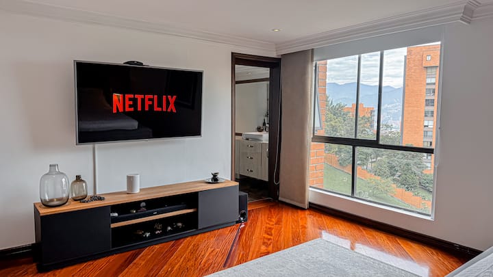 Hlavná izba so svetlou drevenou podlahou, 65-palcovou televíziou s plochou obrazovkou a službou Netflix, nízkym dreveným a čiernym nábytkom, veľkým oknom s výhľadom na mesto a vlastnou kúpeľňou s posuvnými dverami. Moderný a útulný štýl.