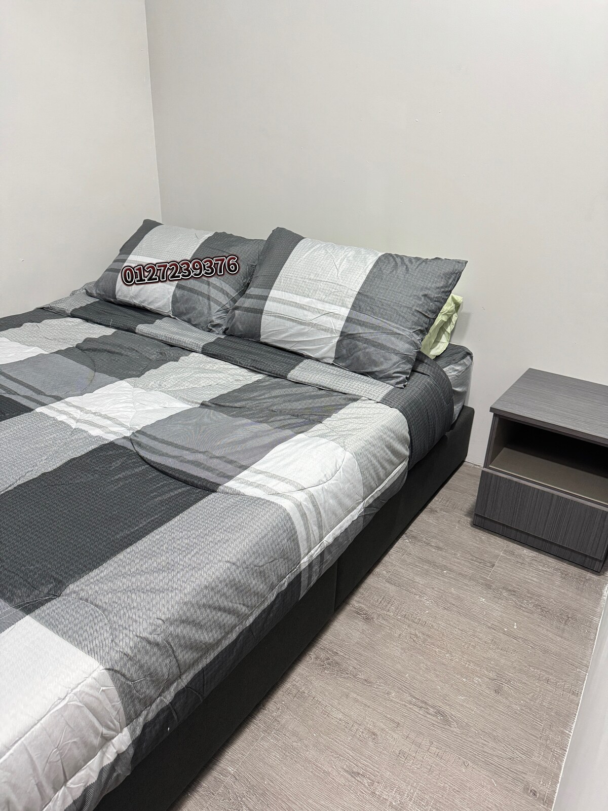 A sleeping area is furnished with a spacious bed dressed in a gray and white patterned duvet. Two pillows are neatly arranged against the headboard. A minimalist nightstand is positioned beside the bed, complementing the light wood flooring.