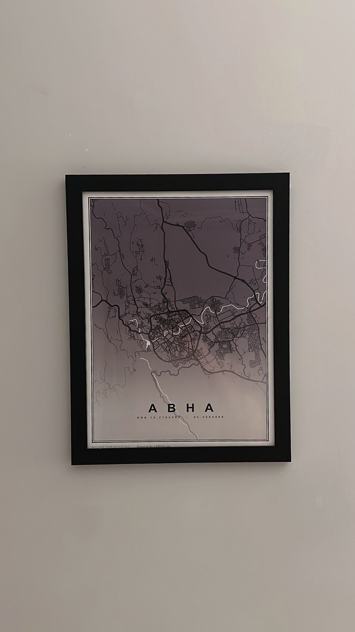 A framed map of Abha is displayed on the wall. The map features a gradient background with shades of purple, and outlines of the city's streets and landmarks are clearly visible in contrasting colors.