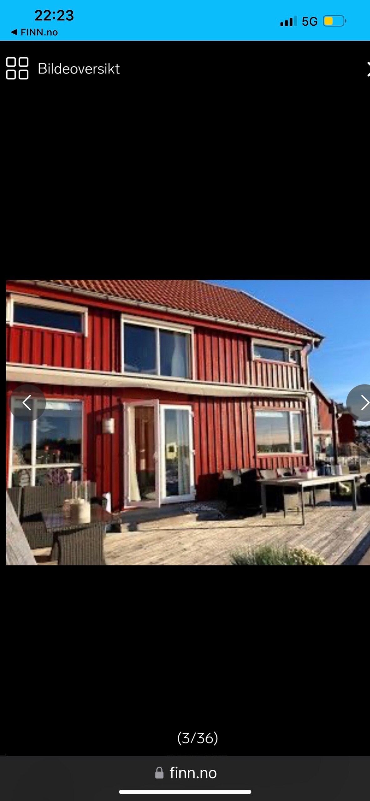 A charming two-story structure with a vibrant red exterior features a spacious deck lined with outdoor furniture. Large windows allow natural light to fill the interior, creating an inviting space for relaxation. The clear sky reflects the tranquil atmosphere of the surroundings.