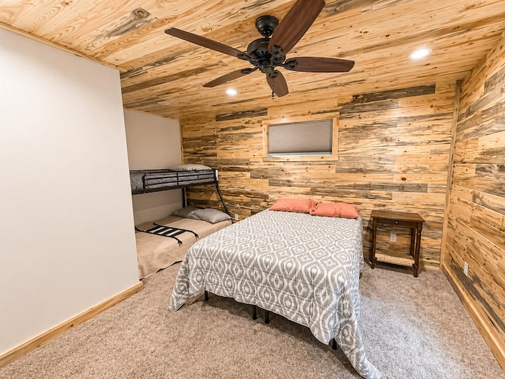 Esta habitación familiar cuenta con una acogedora cama tamaño queen y literas de dos camas individuales, ideal para niños o invitados adicionales. Rodeado de cálidos tonos de madera, iluminación empotrada y un ventilador de techo, es la mezcla perfecta de comodidad y encanto rústico.