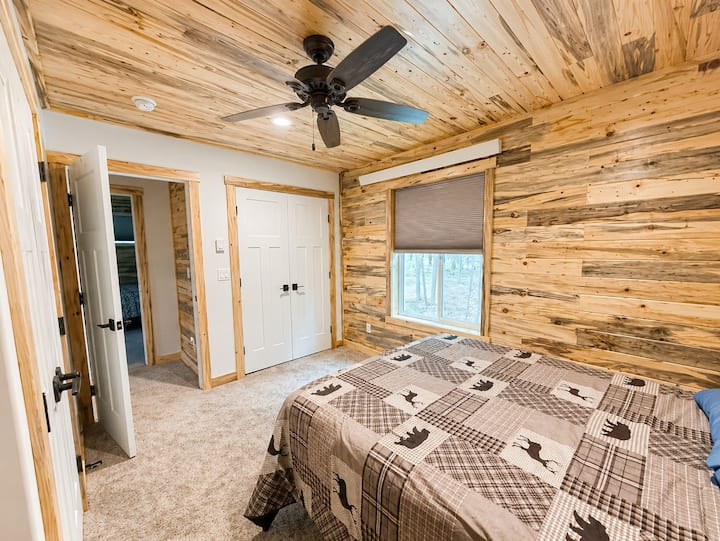 Este acogedor dormitorio con temática de bosque cuenta con una cómoda cama tamaño queen, paneles de madera rústica, alfombra de felpa y un ventilador de techo. Las grandes ventanas ofrecen vistas tranquilas al bosque, mientras que el espacioso armario proporciona mucho espacio de almacenamiento para una estancia más larga.