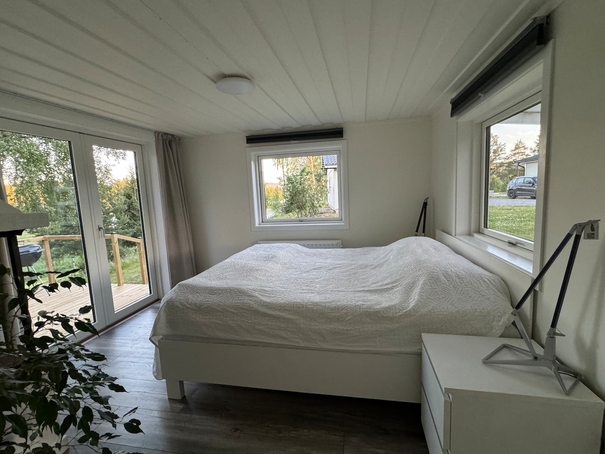 Slaapkamer met het beste uitzicht! Grote ramen en deuren die openen naar een terras en gazon omgeven door bomen en uitzicht op het meer. Het meer ligt op een paar stappen afstand 