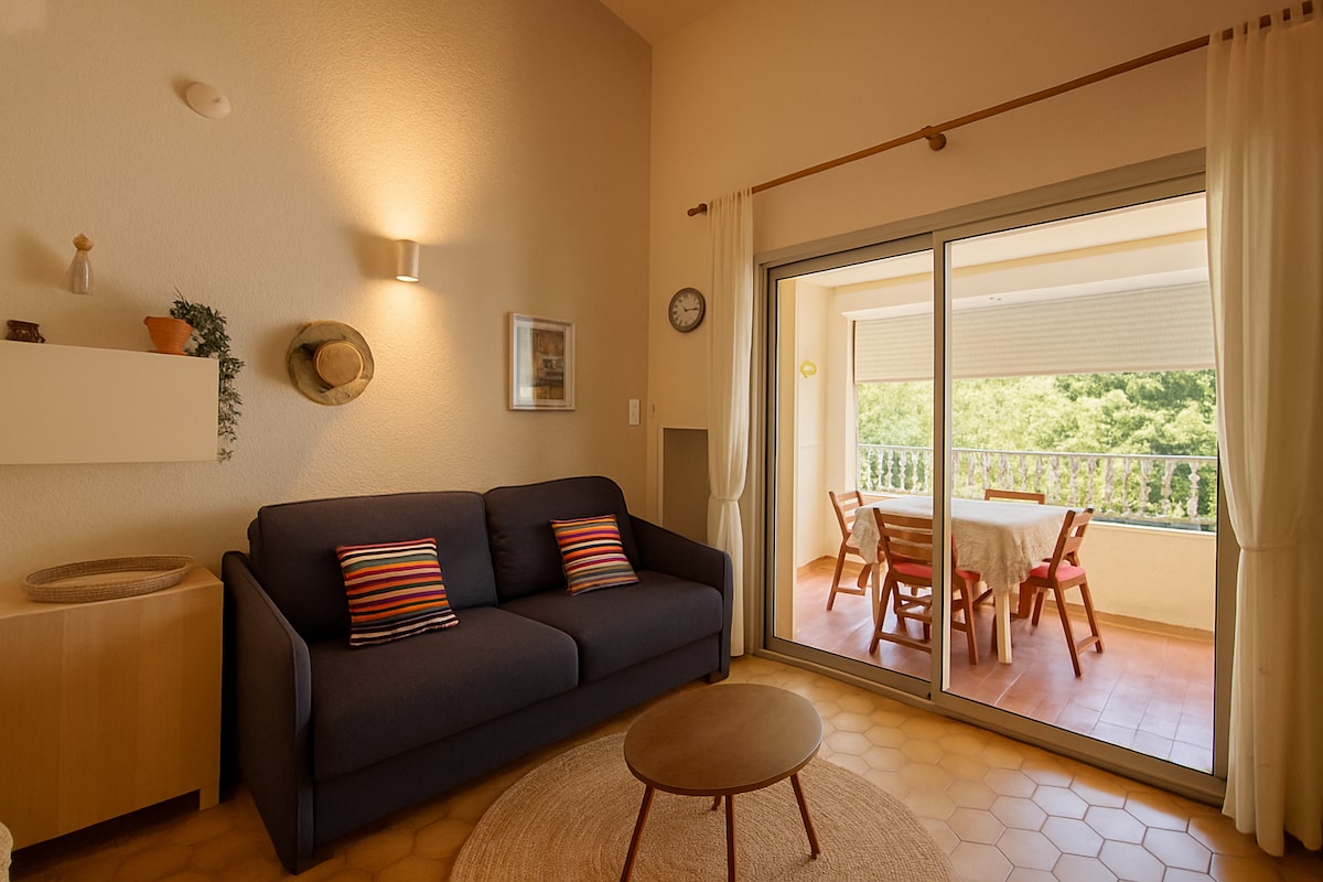 A living area is presented with a navy sofa adorned with colorful cushions, complemented by a round coffee table. Natural light floods the space through large sliding glass doors, leading to a balcony with a dining table and chairs, framed by greenery.
