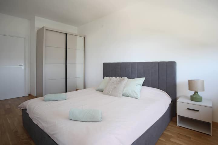 Un dormitorio con una gran cama doble, una mesita de noche, un armario, persianas y una salida a la terraza