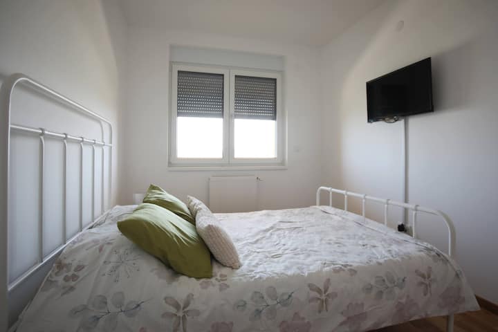 Segundo dormitorio con una cama doble, persianas, TV y mesita de noche.
