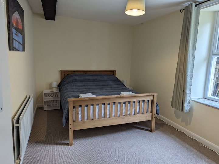 Брачна спална соба на долниот кат со ноќни масички, светилки и мал фиокар со огледала и радијатор