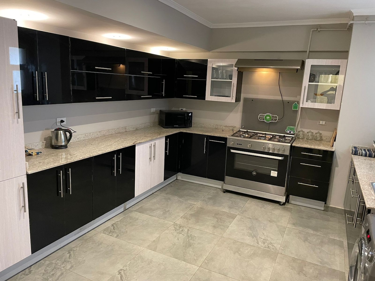 The kitchen features a modern design with sleek black and light wood cabinetry. A spacious granite countertop offers ample prep space, complemented by stainless steel appliances, including a gas stove and microwave. Natural light illuminates the area, enhancing its functional layout.