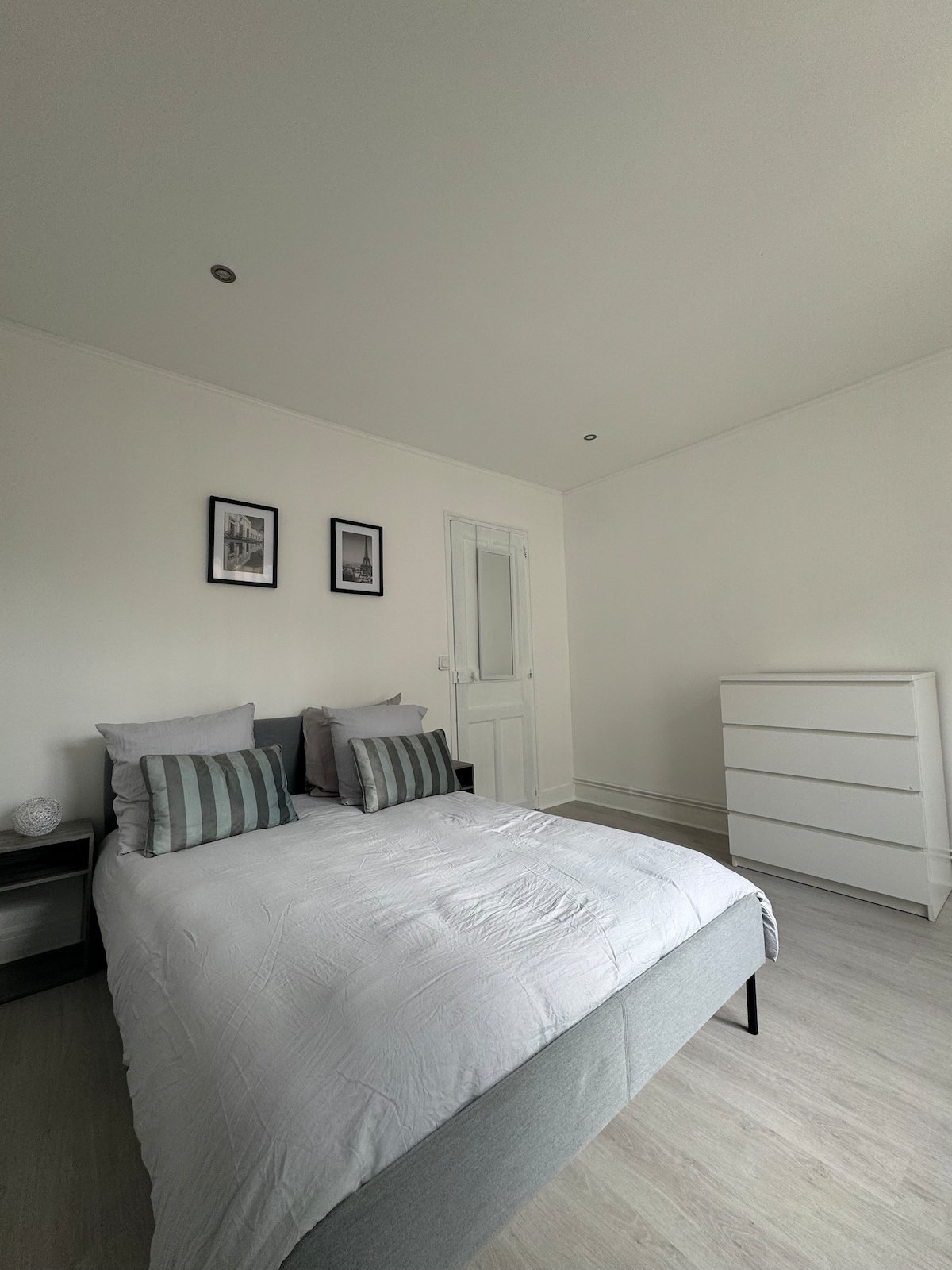 אזור שינה עם מיטה זוגית, שידות ליד המיטה, מדף אחסון וציור דקורטיבי.