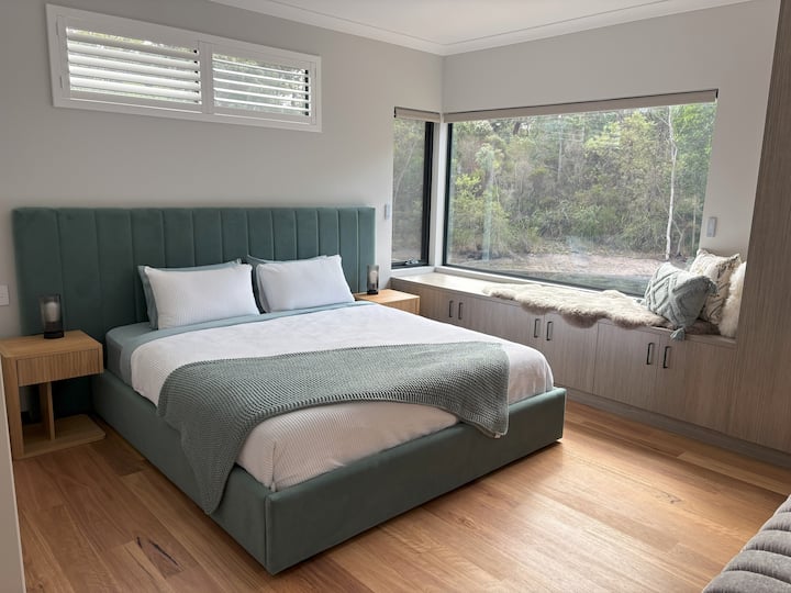 Luxurious King Bed with plush upholstered headboard and fitted with soft linen sheets and a cosy feather and down quilt. This space combines contemporary design with nature's beauty, making it an ideal haven for rest and rejuvenation.