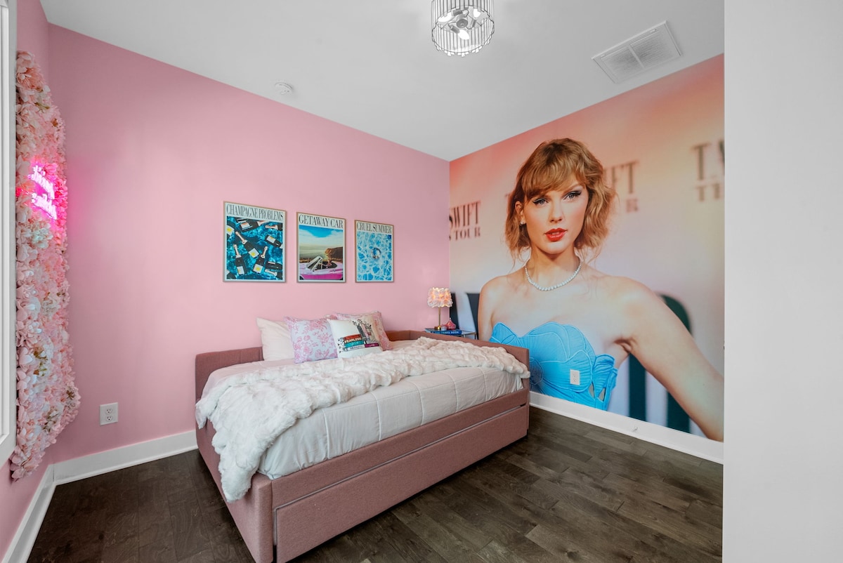 The Taylor Swift bedroom features a trundle bed with both full and twin mattresses, plush luxury linens, a vibrant Taylor wall mural, and playful neon accents—perfect for fans and a fun, cozy stay!