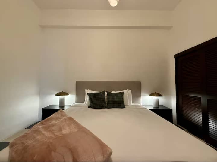 غرفة نوم رئيسية مريحة مع سرير فاخر وإضاءة دافئة.