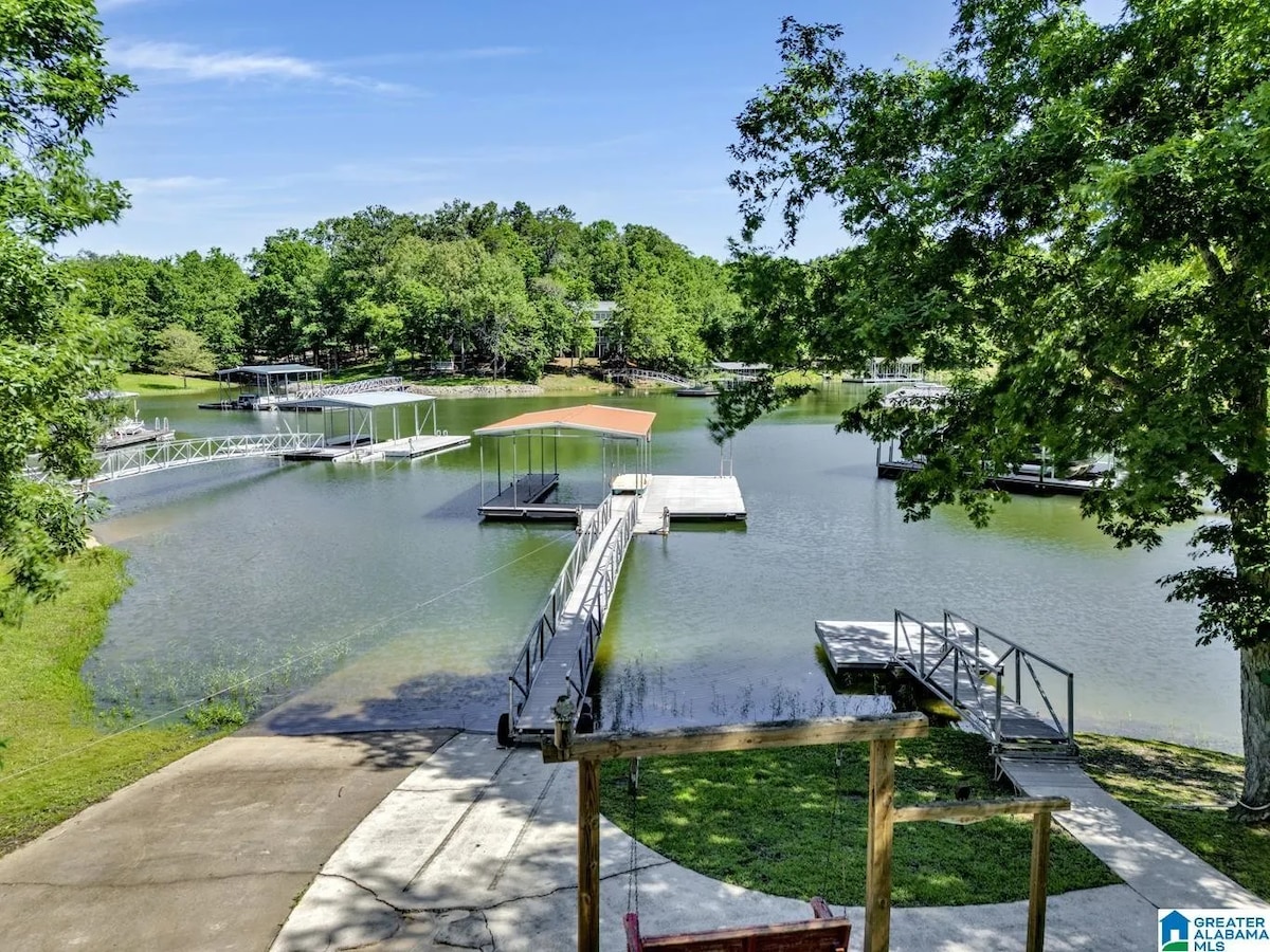 A serene lakeside view is captured, featuring calm waters surrounded by lush greenery. Wooden docks extend into the water, providing access for boating and fishing. Sunlight reflects off the surface, enhancing the peaceful atmosphere of the surrounding landscape.
