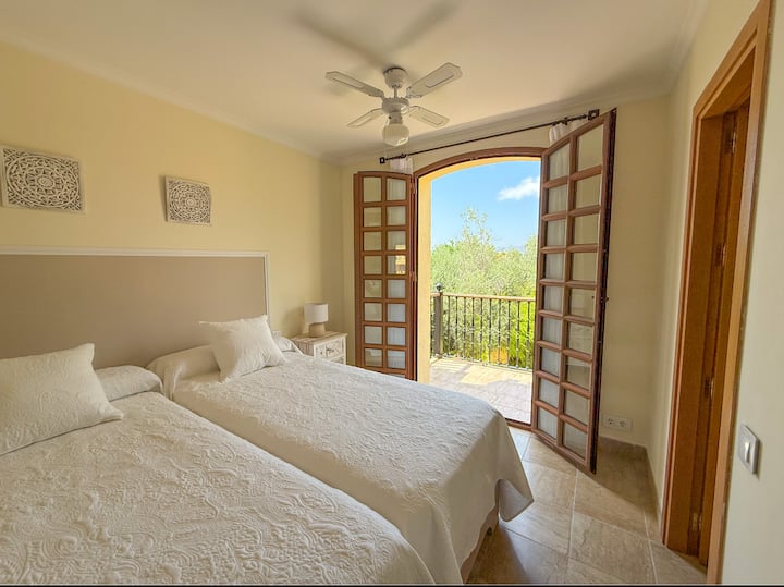 Habitación en suite con cama doble, ventilador de techo y balcón al resort.