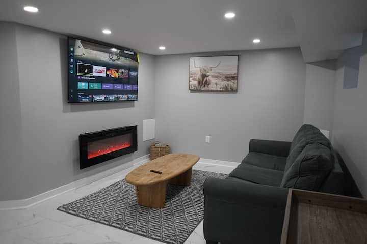 Priestranná obývacia izba v suteréne s rozkladacou pohovkou, nástenným televízorom, elektrickým krbom a štýlovým konferenčným stolíkom – ideálna ako ďalší priestor na spanie alebo útulné útočisko.