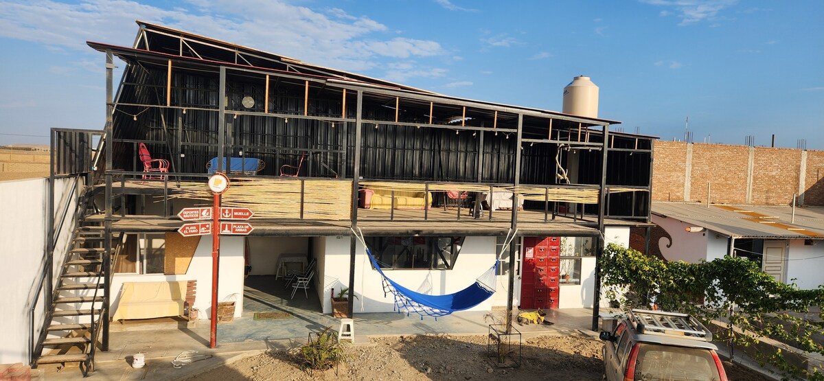 A two-story building showcases a large deck with seating areas illuminated by natural light. A hammock is suspended on the lower level, while an outdoor staircase provides access to the upper deck. Surrounding vegetation adds a touch of greenery to the setting.