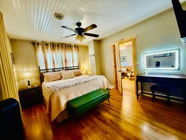 King bedroom with hardwood floors, ceiling fan, bedside lighting, and a modern vanity. A comfortable, inviting space to relax during your stay.