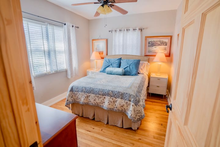 Inviting queen bedroom with natural light, hardwood floors, and soft bedside lamps. Clean, comfortable space for a restful stay.